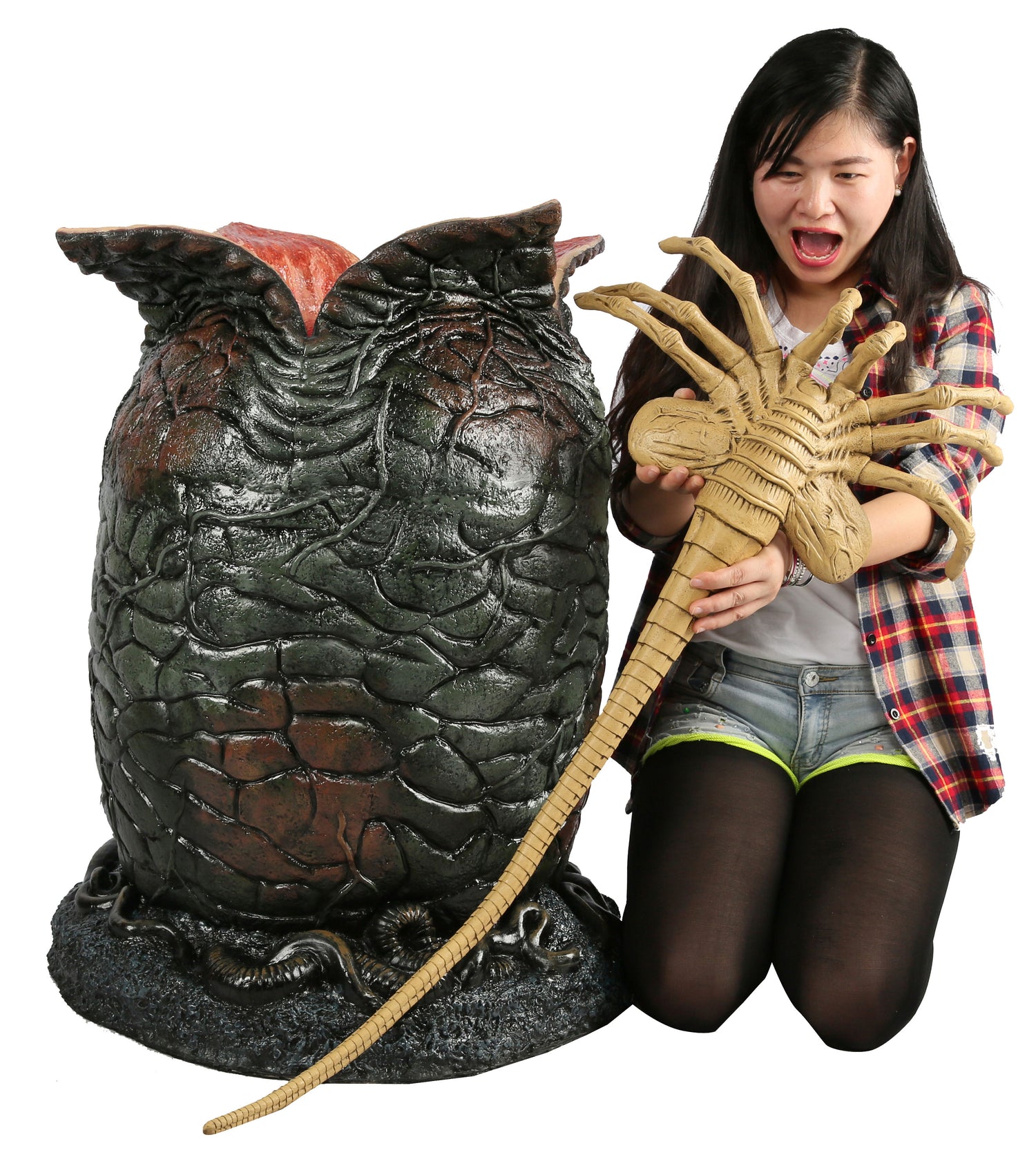 Woman holding life-size Facehugger sitting next to life-size Xenomorph egg
